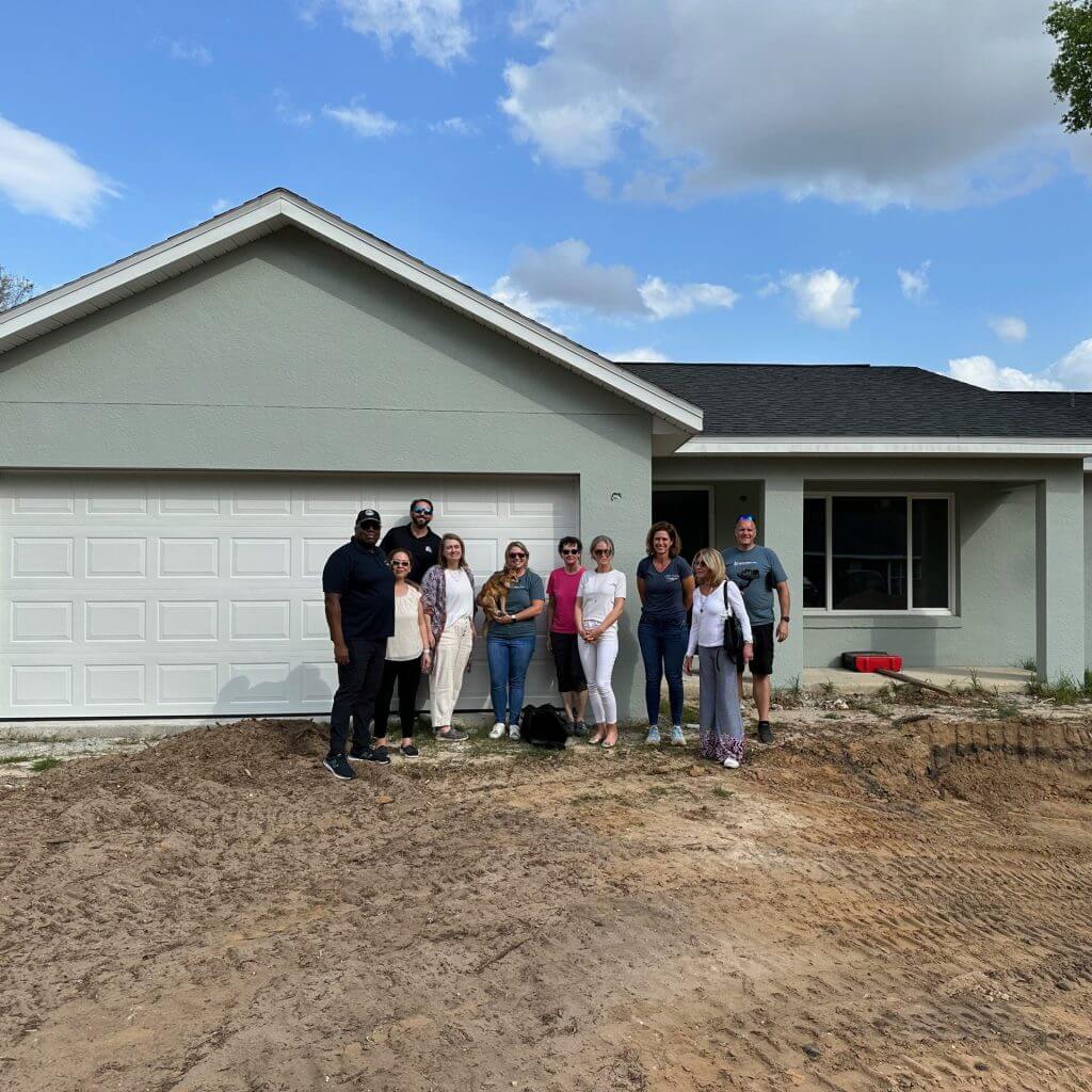 Grant Anderson from RealWealth stands in front of a house with a group of real estate investors. 