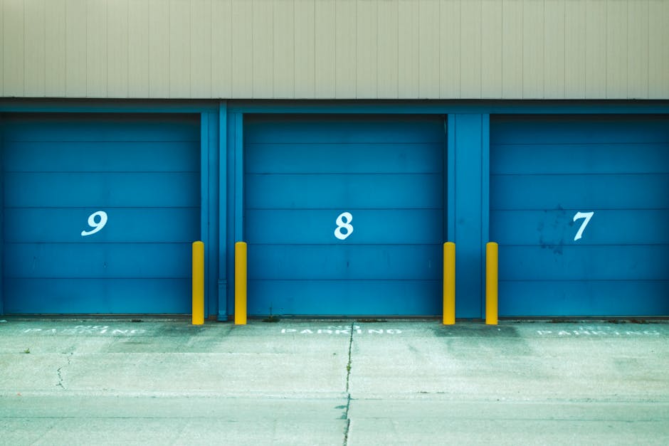 Three blue self-storage doors numbered 9, 8, and 7 with yellow barriers in urban environment.